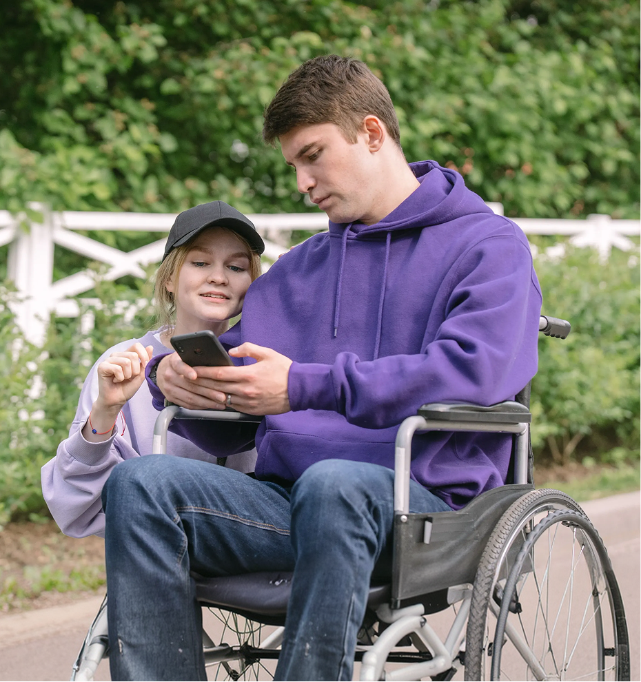 Person in wheelchair looking at a phone with a friend outdoors