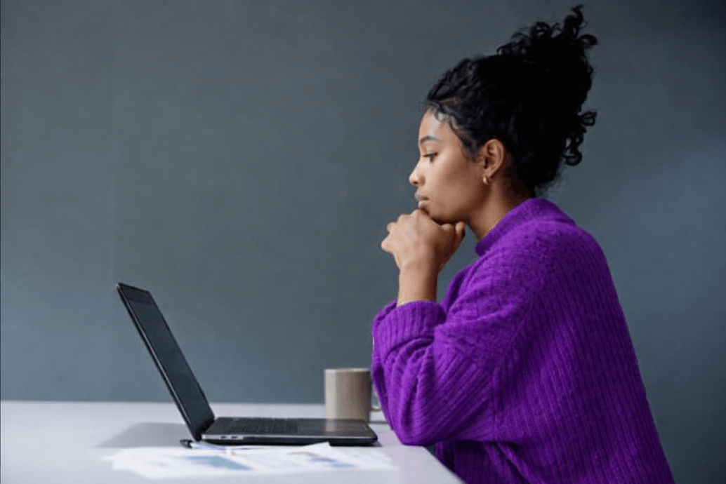 Woman sitting at a desk reviewing a website on a laptop, focused on evaluating accessibility and usability.