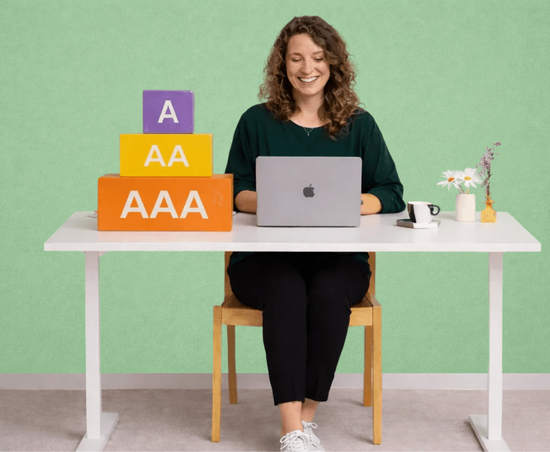 Woman sitting at a desk using a laptop with stacked blocks labeled A, AA, and AAA representing WCAG accessibility levels.